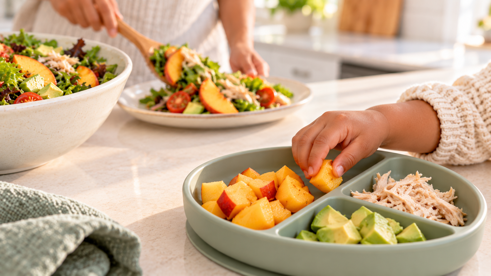 A child reaches for peaches from a divided toddler plate in the foreground while a caregiver serves a family meal